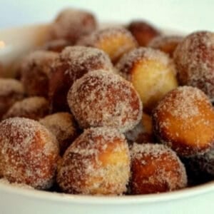 A bowl piled high with warm sourdough donut holes rolled in cinnamon sugar, with their crisp edges and soft centers visible up close.