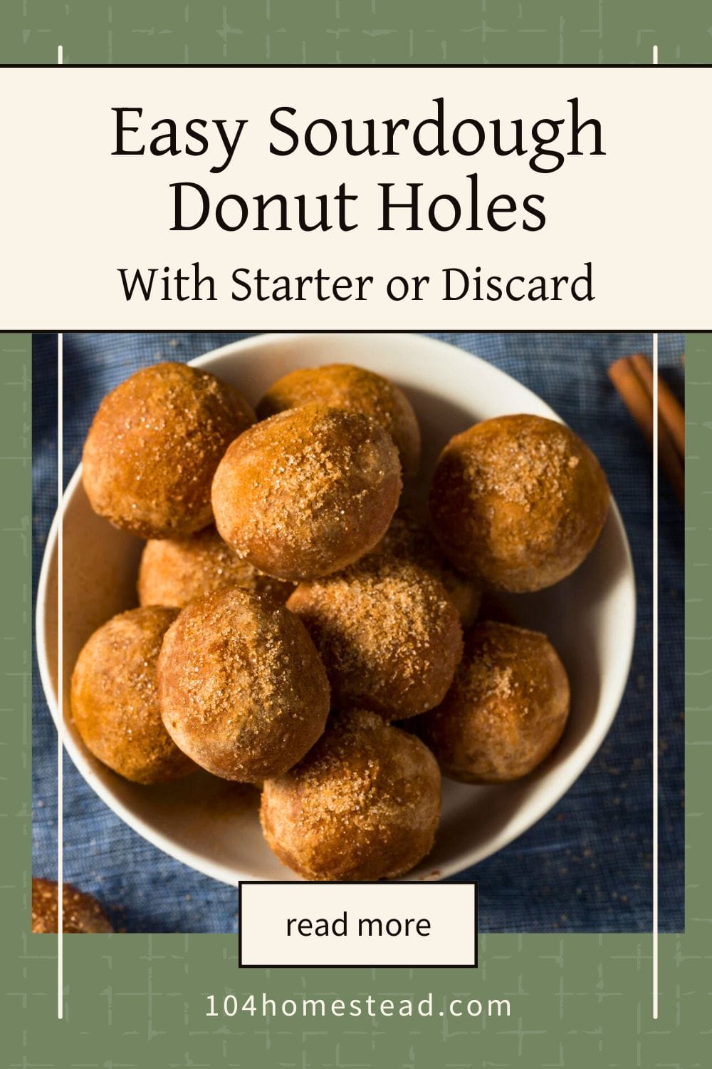 A white bowl filled with golden-brown sourdough donut holes coated in cinnamon sugar, sitting on a blue cloth with cinnamon sticks in the background — a cozy homemade treat made with sourdough starter or discard.