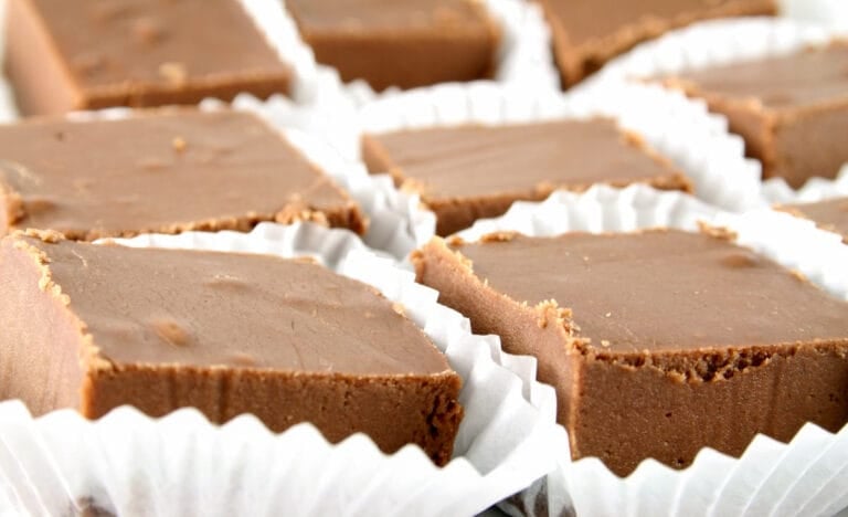 Rows of creamy, chocolate fudge squares in white paper liners, ready to serve or package.
