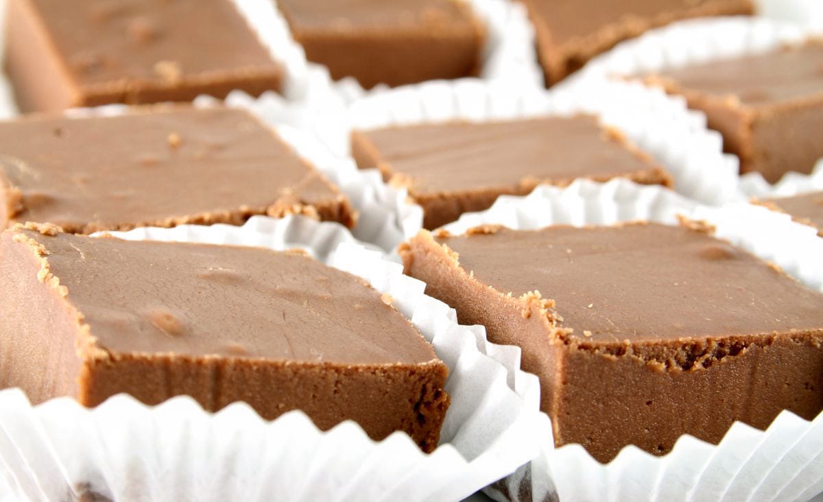 Rows of creamy, chocolate fudge squares in white paper liners, ready to serve or package.