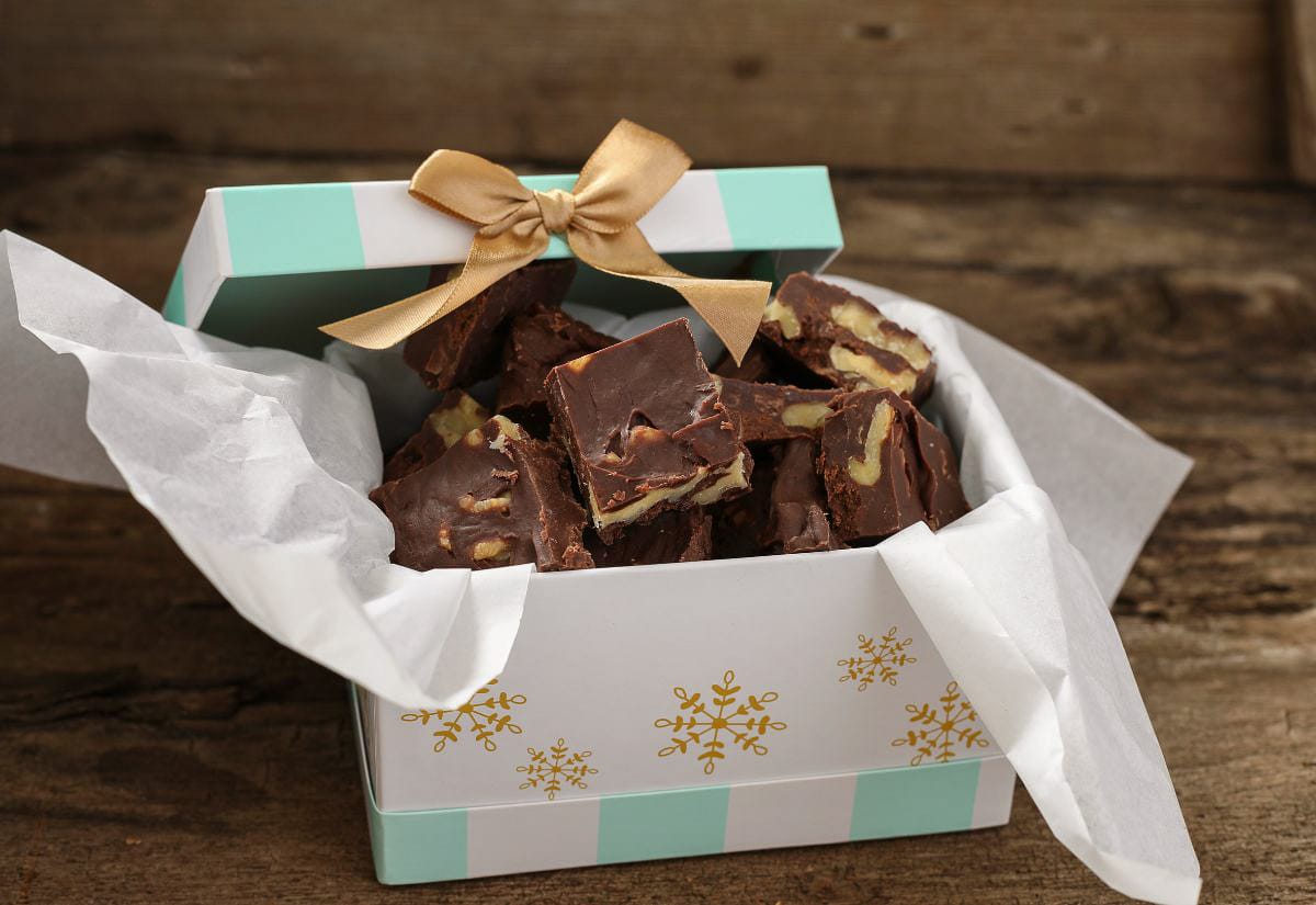 Gift box filled with easy homemade fudge topped with chopped nuts, wrapped in parchment and tied with a gold ribbon.