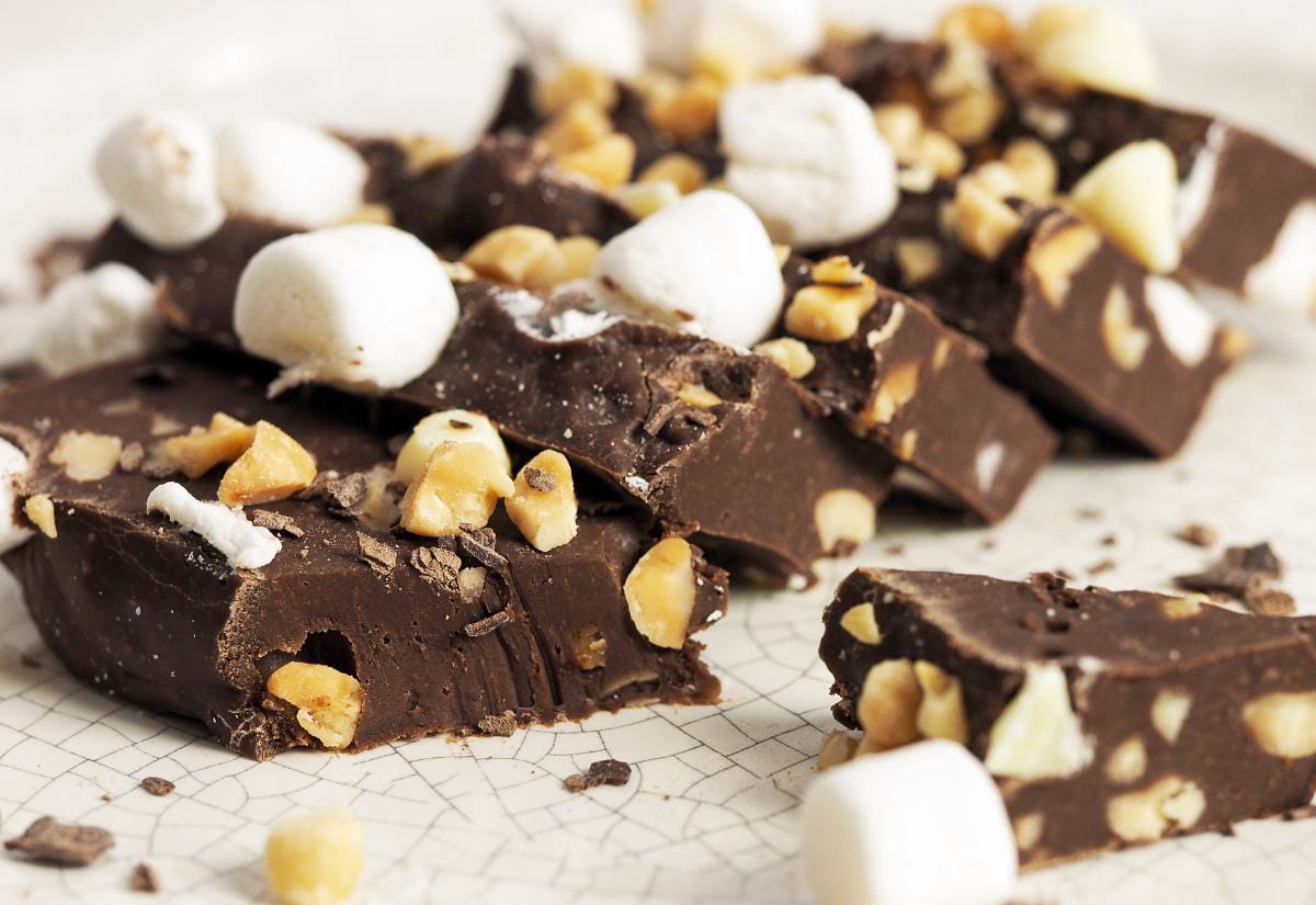 Close-up of rocky road-style homemade fudge with marshmallows and chopped nuts on a light speckled background.