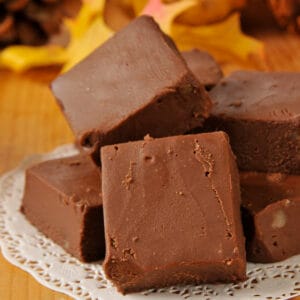 Close-up of rich, chocolatey squares of easy homemade fudge stacked on a white doily.