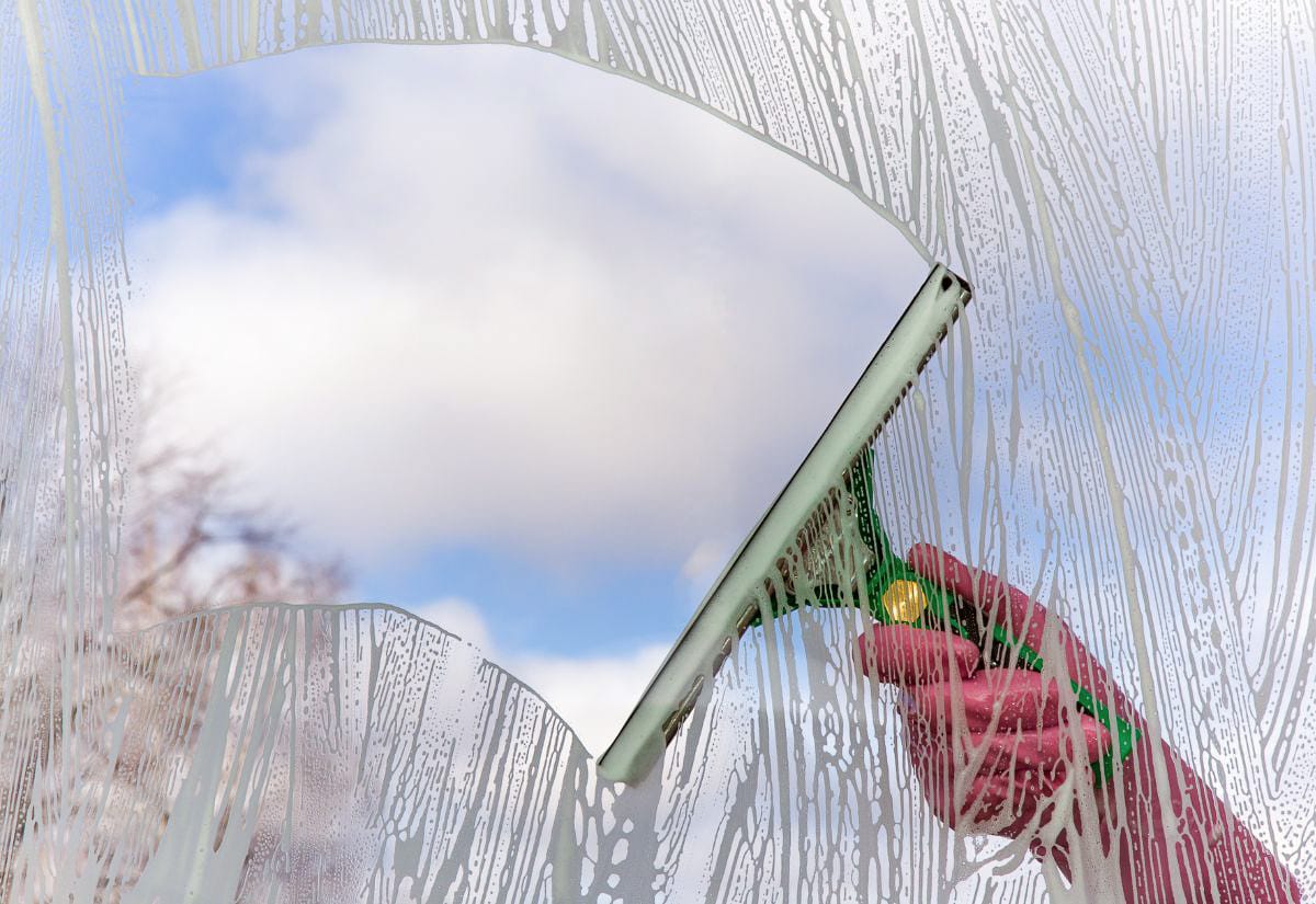 Close-up of a squeegee pulling soapy water down a window, leaving a clear, streak-free section of glass behind.