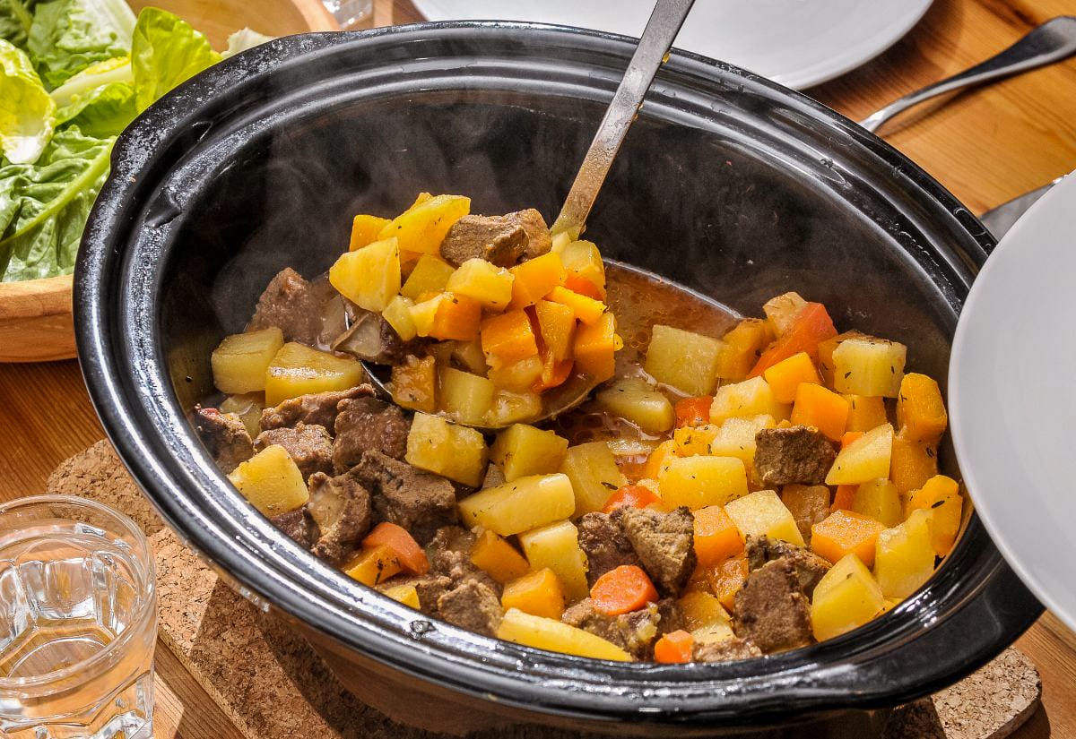 Hearty beef and root vegetable stew simmering in a slow cooker, filled with chunks of potato, carrot, and meat being ladled into a bowl.