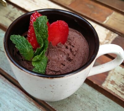 Sweet potato chocolate mousse in a cream speckled coffee mug, decorated with fresh strawberries and mint leaves.
