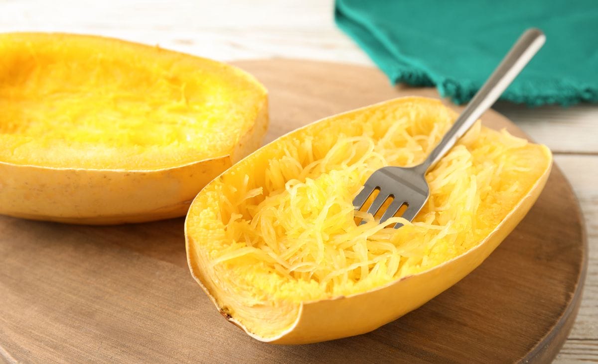 A cooked spaghetti squash on a cutting board with a fork making noodles.
