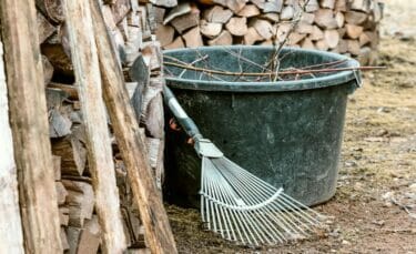 A large black rubber bucket filled with sticks and a rake sitting next to the wood pile.