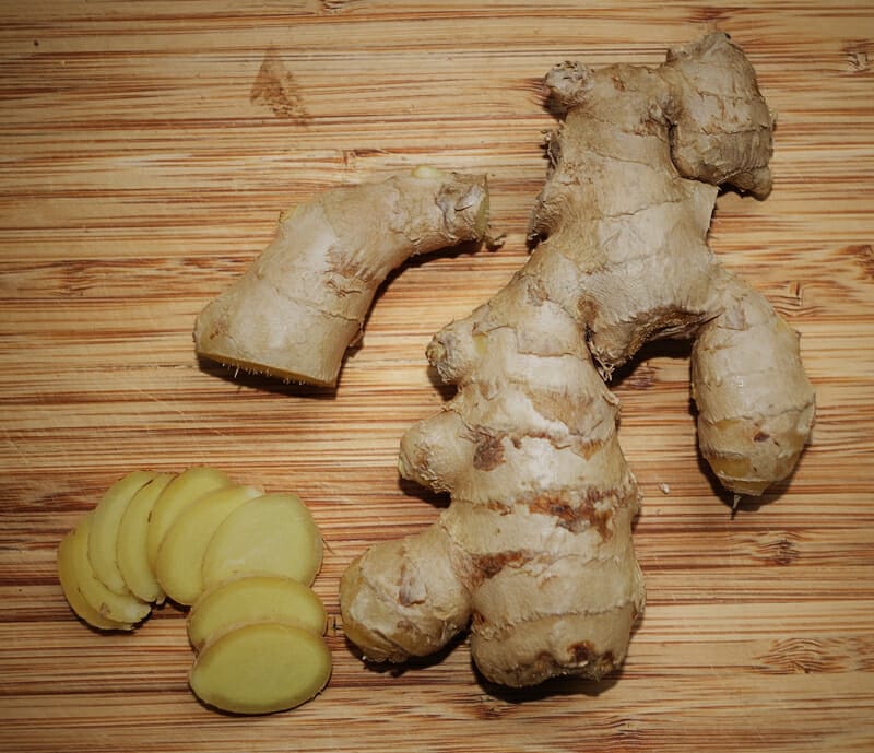 Fresh ginger root with several slices on a wooden cutting board.