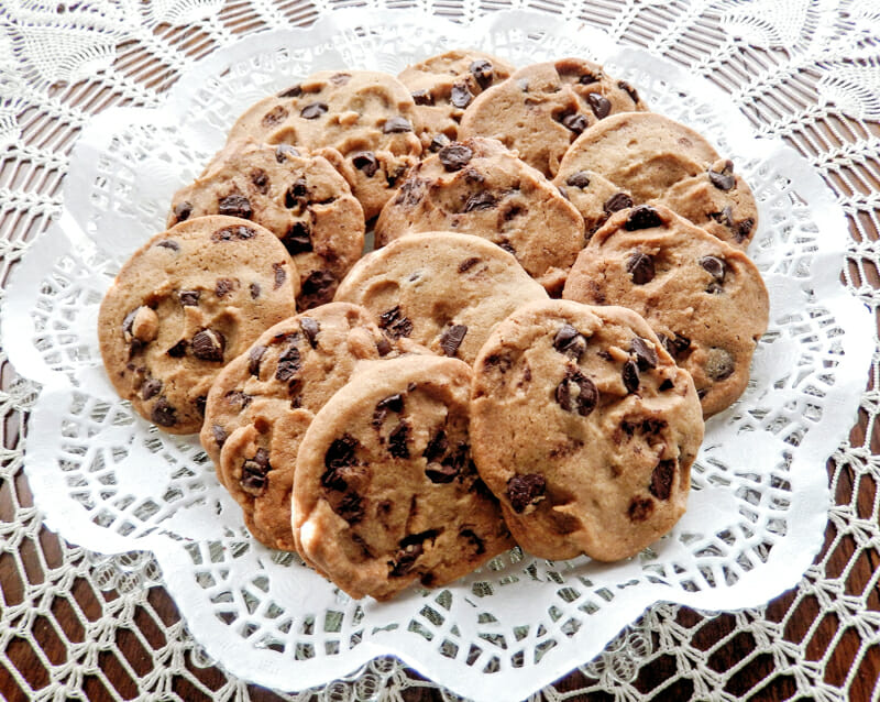 A dozen chocolate chip cookies spread out on a white doily. 
