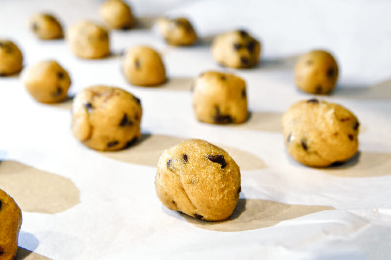 1" balls of chocolate chip cookie dough on parchment paper.