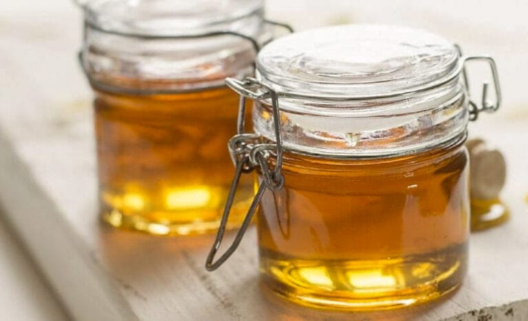 Two small glass jars filled with amber-colored homemade cough syrup sitting on a light wooden surface, showing the warm color and simple, natural look of the honey-based remedy.