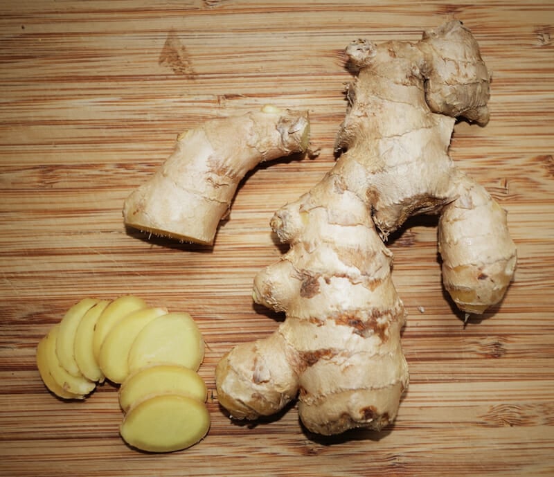 Ginger root sliced thin on a bamboo cutting board.