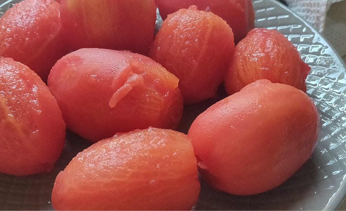 Close-up view of several peeled tomatoes on a plate, their skins removed cleanly after freezing and warming, ready to be canned or cooked.