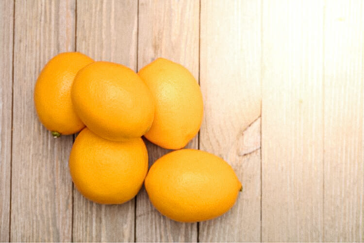 Five Meyer lemons sitting on a wood table.