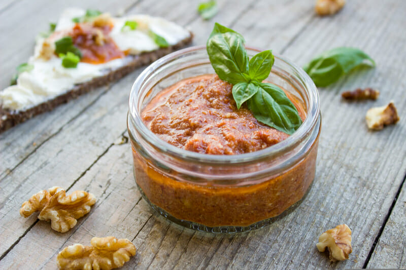 Tomato pesto in a glass jar, garnished with basil, and a piece of pita bread beside it.