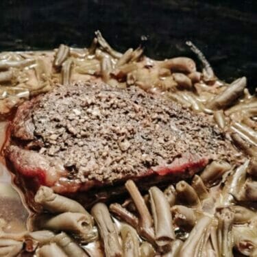 A close up view of roast beef sitting on green beans.