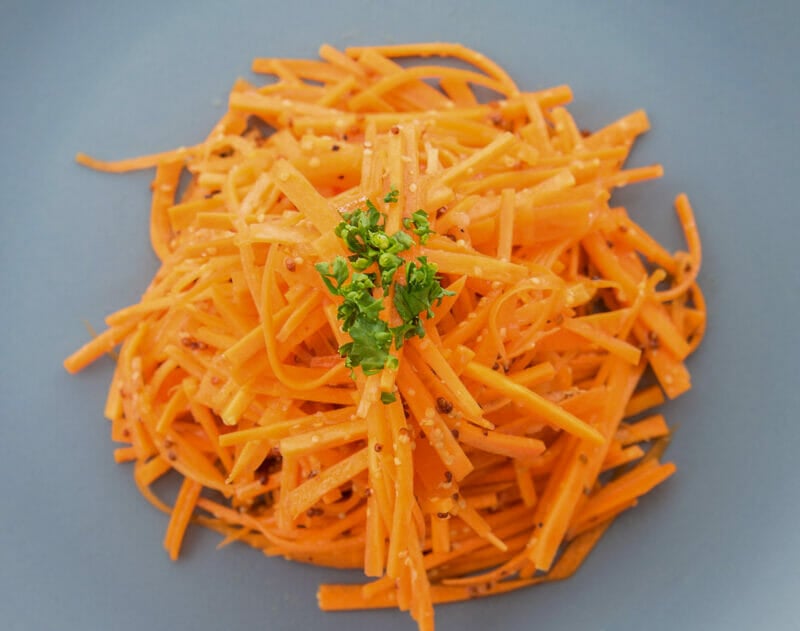 Carrot salad on a blue plate, topped with fresh parsley.