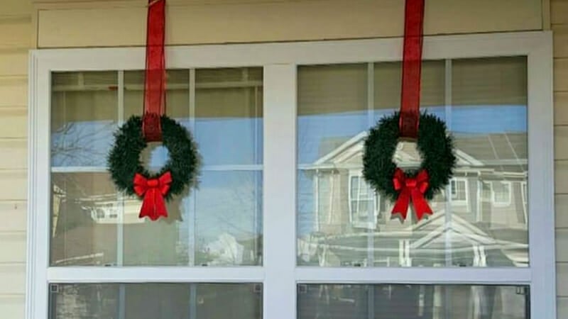 Two basic wreaths hanging from red ribbons in front of windows.