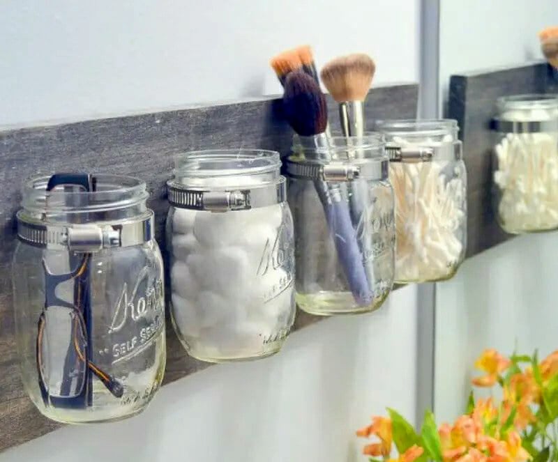 Eyeglasses, cotton balls, makeup brushes, and cotton swabs stored in mason jars attached to a piece of barnwood.