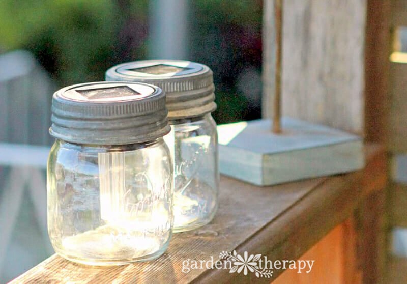 Mason jars with solar lights in the lid charging on a porch railing.