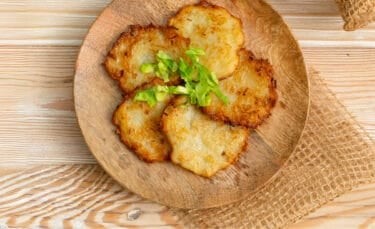 Golden brown potato pancakes with instant mashed potatoes served on a rustic wooden plate, topped with fresh green garnish.