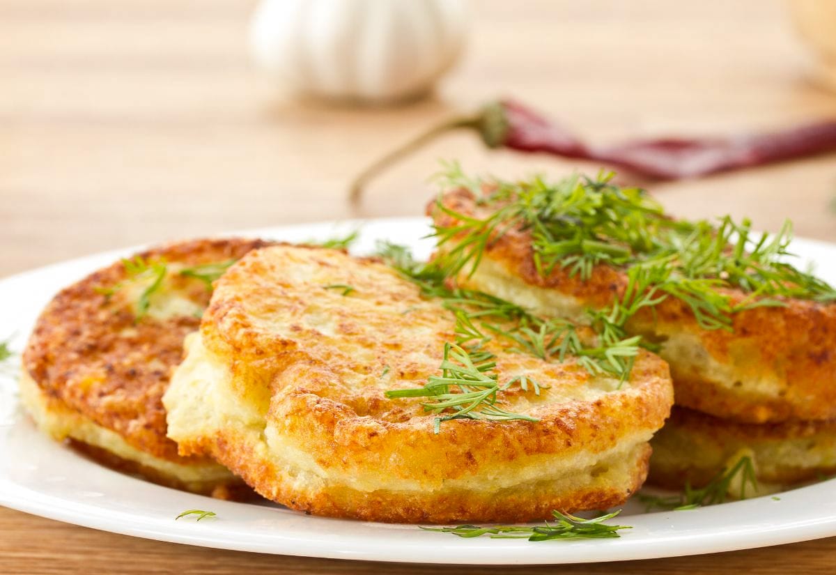 Close-up of crispy potato pancakes with instant mashed potatoes on a white plate, sprinkled with fresh dill for garnish.