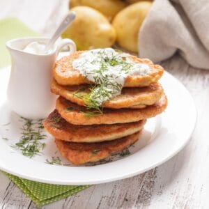 A stack of golden potato pancakes topped with fresh dill and served with sour cream on the side.