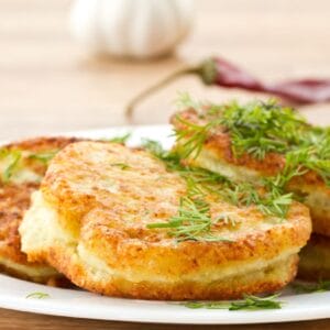 Golden brown potato pancakes garnished with fresh dill, served on a white plate.