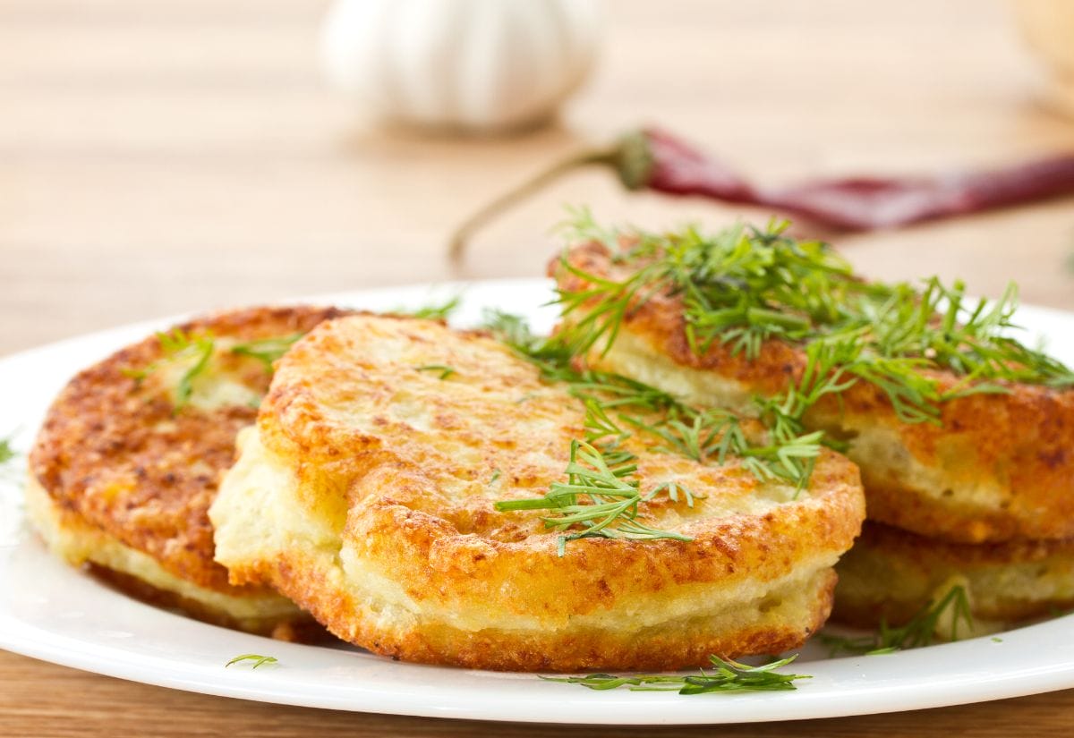 Golden brown potato pancakes garnished with fresh dill, served on a white plate.