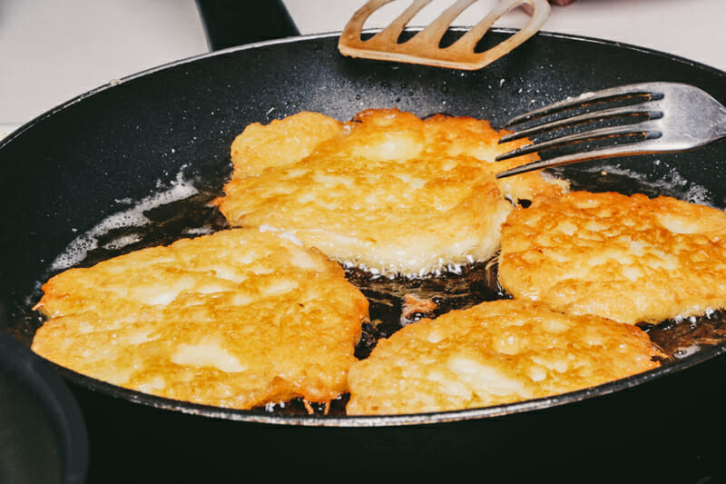 Four potato pancakes frying in a skillet.