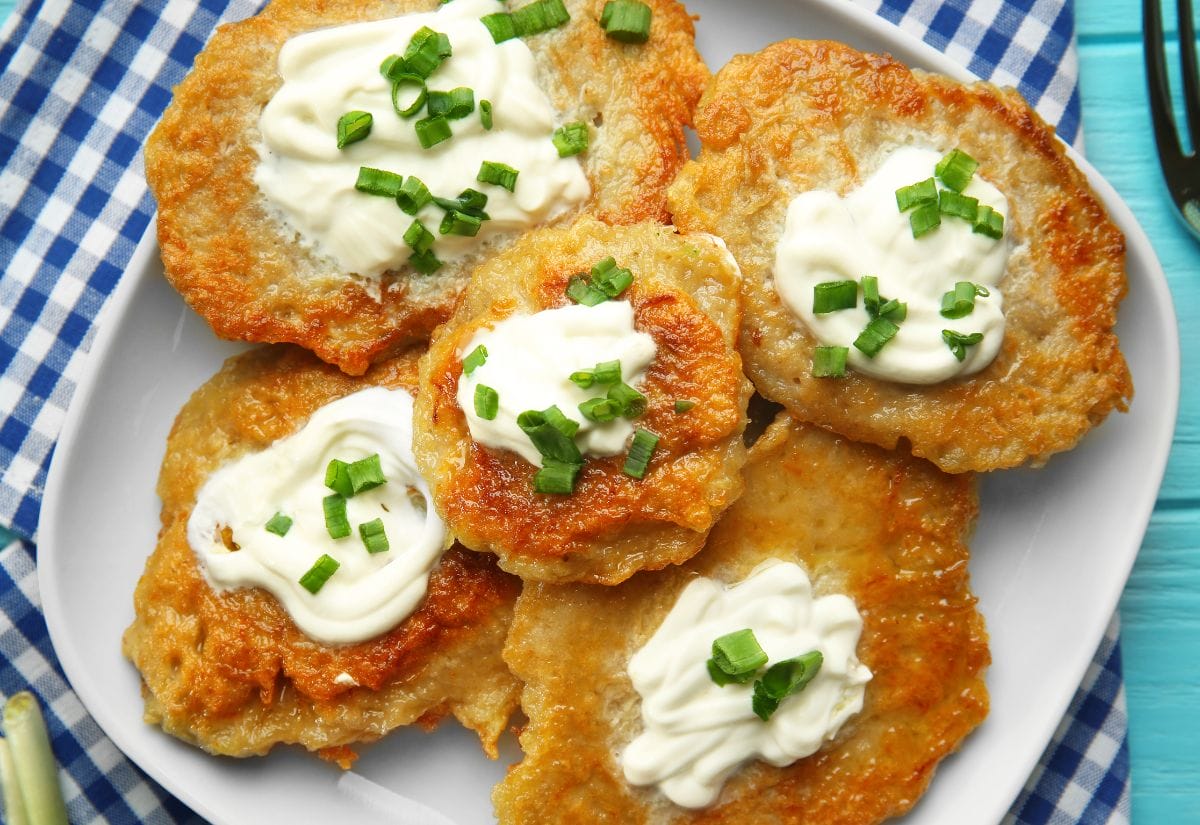 A plate of potato pancakes topped with sour cream and chopped green onions, set on a checkered blue napkin.