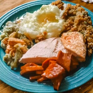 Plate of reheated Thanksgiving leftovers with sliced turkey, mashed potatoes, gravy, green bean casserole, stuffing, and glazed carrots, showing the cozy comfort of a second-day meal.