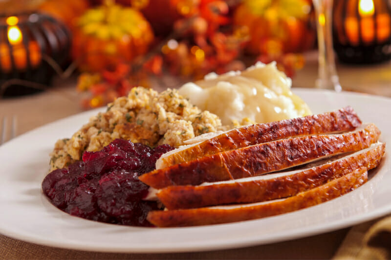 Sliced turkey on a plate with mashed potatoes, stuffing, and cranberry sauce.