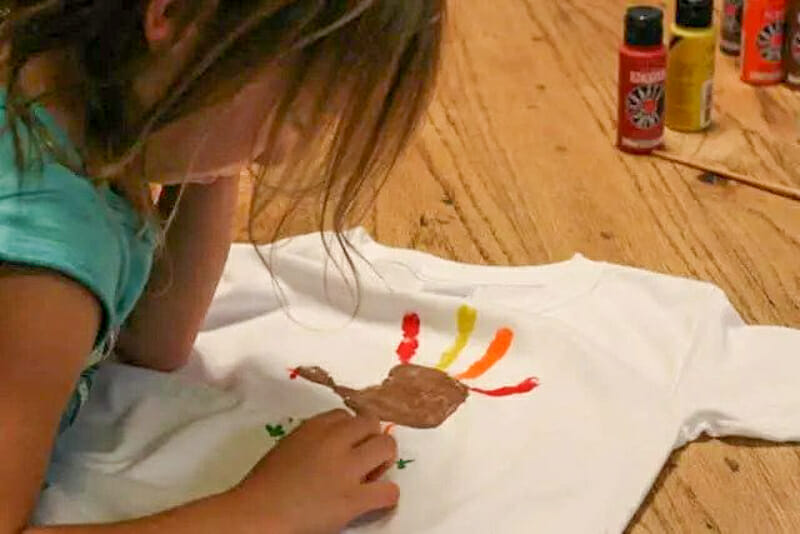 A child adding detail to their handprint turkey t-shirt.