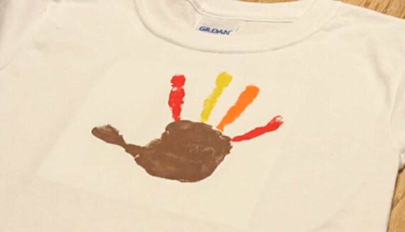 A turkey colored handprint on a white t-shirt.