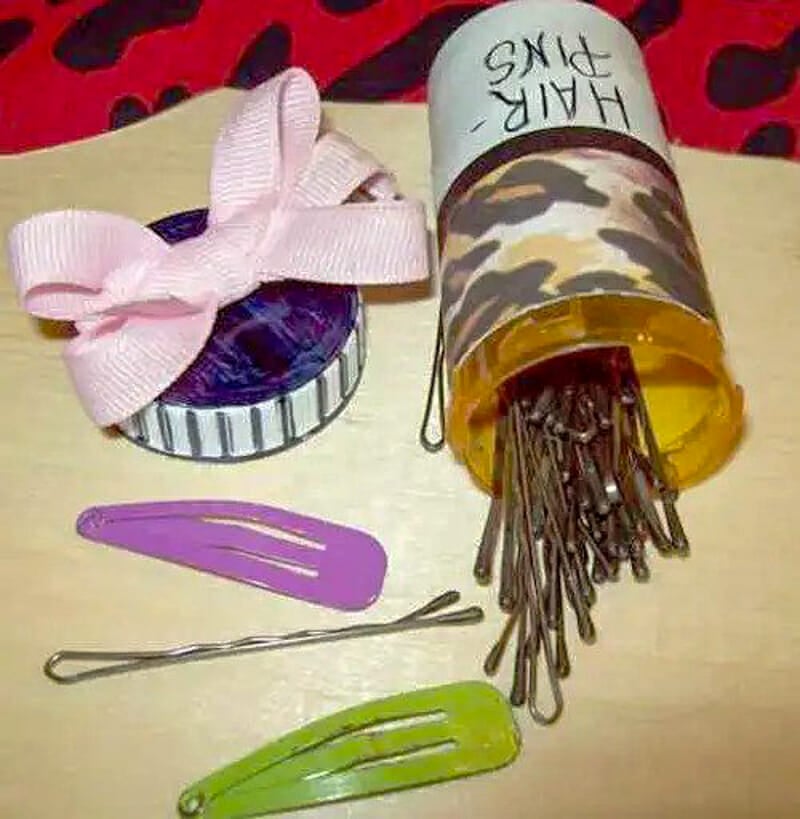A pill bottle filled with bobby pins and a purple hair clip.