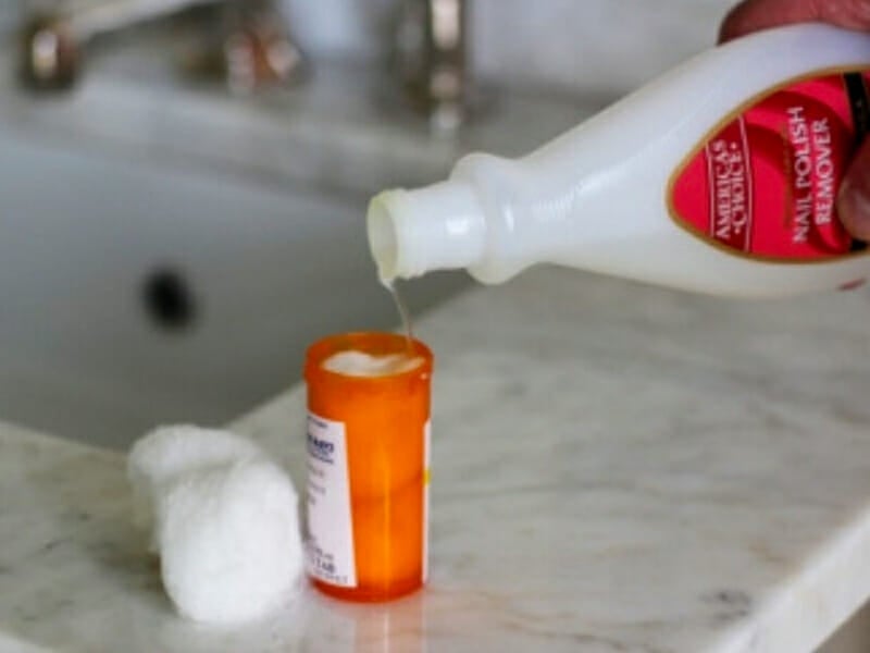 Pouring nail polish remover into a pill bottle filled with cotton balls.