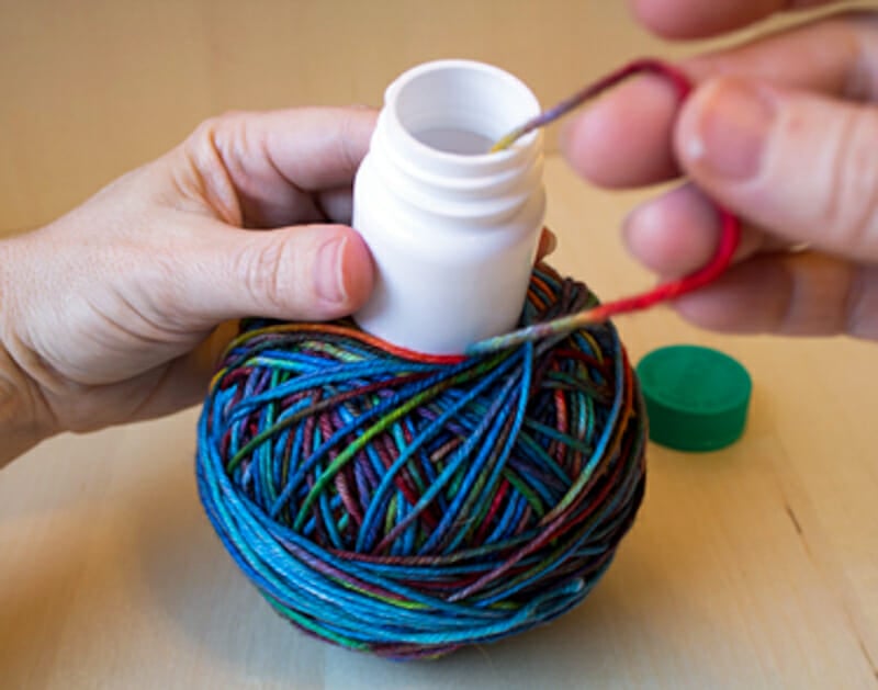 A multicolored ball of yarn wrapped around a white medicine bottle.