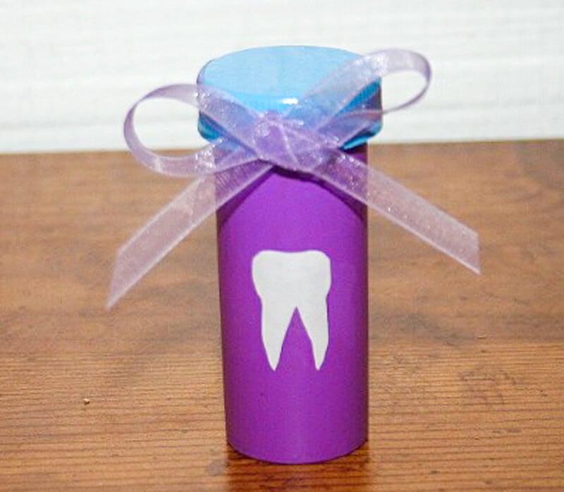 A pill bottle painted purple and blue with a purple ribbon and a tooth sticker on the front.