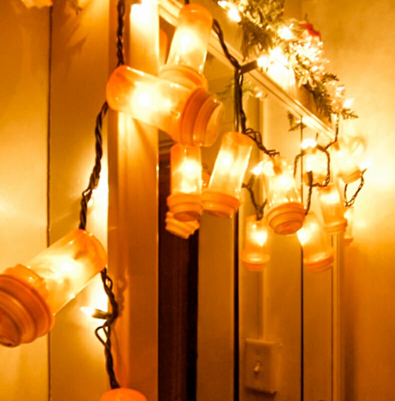 A string of lights hung on a mirror with pill bottles secured over the bulbs.