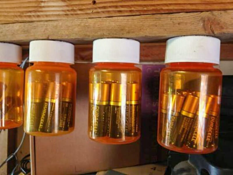 Pill bottles filled with batteries fastened to a piece of wood by their lids.