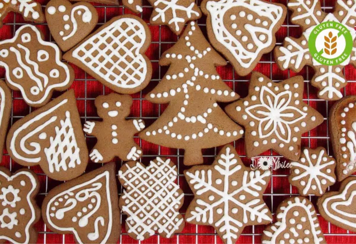 A cooling rack filled with gluten-free gingerbread cookies in festive shapes like stars, hearts, and trees, each decorated with simple white royal icing patterns over a red background.