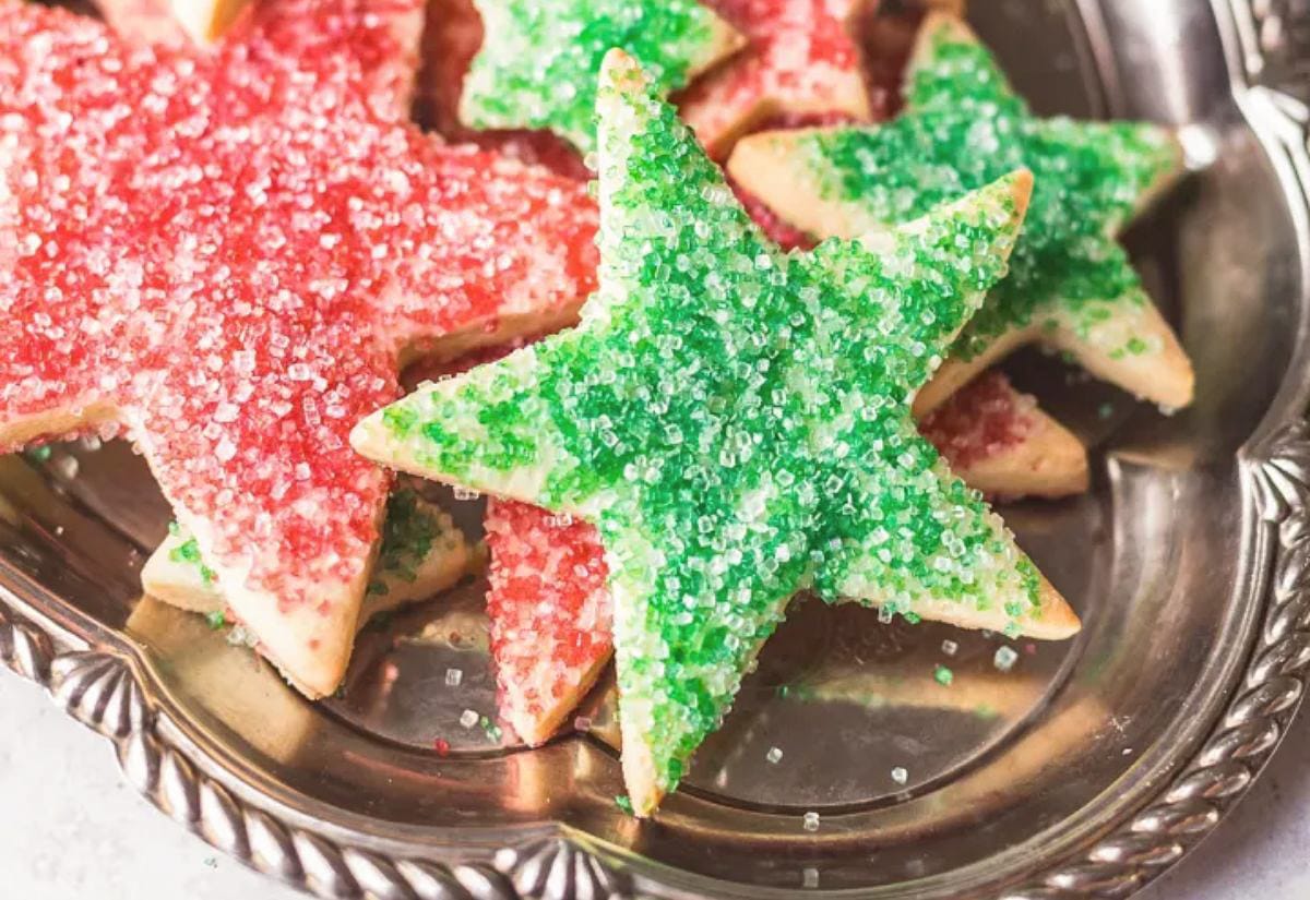 Star-shaped sugar cookies coated in bright red and green sanding sugar, arranged on a vintage silver tray.