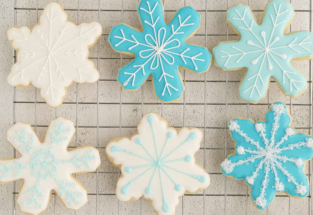 Iced snowflake cookies in shades of white and icy blue, decorated with delicate royal icing details and cooling on a wire rack.