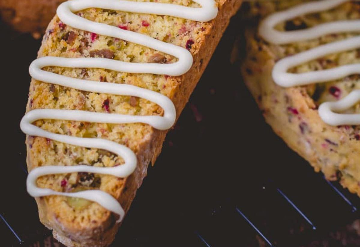 Slices of cranberry pistachio biscotti topped with a simple white icing drizzle, resting on a cooling rack.