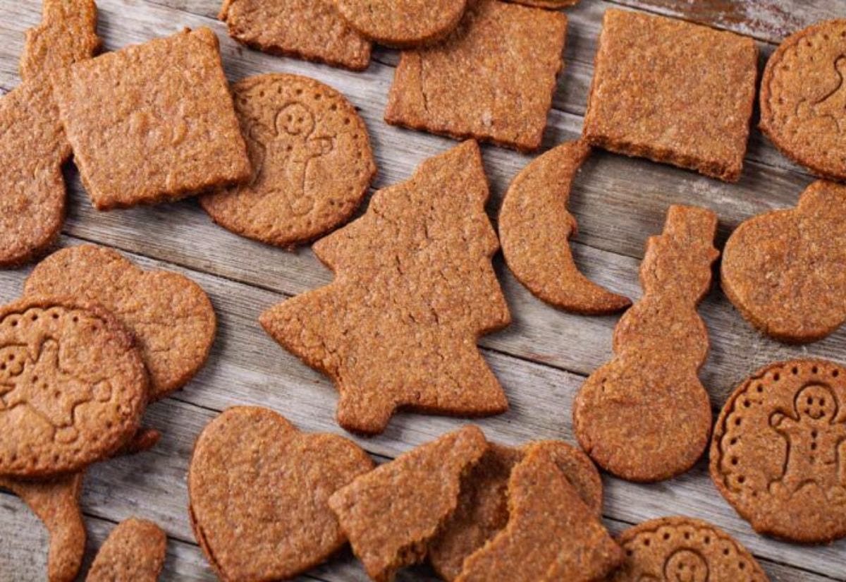 Assorted stamped spice cookies in shapes like trees, hearts, snowmen, and circles, laid out on a rustic wooden surface.