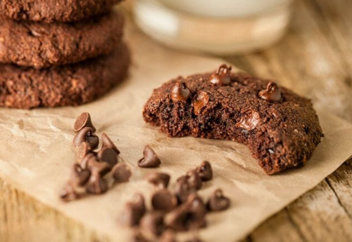 A soft double-chocolate cookie with a bite missing, surrounded by chocolate chips on parchment paper.