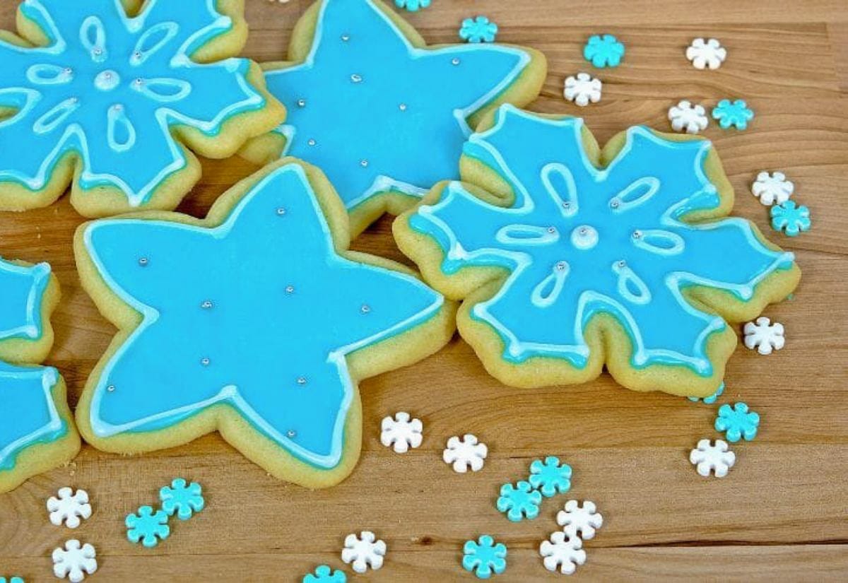 Blue and white snowflake sugar cookies decorated with royal icing, arranged on a wooden surface with matching snowflake sprinkles.