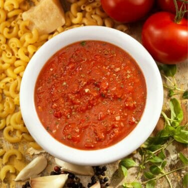 Homemade spaghettis sauce in a white bowl with ingredients surrounding it.